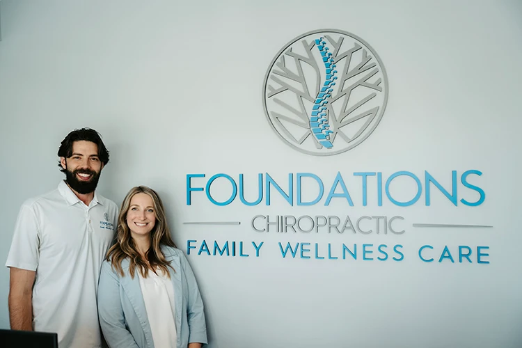 Chiropractor Zionsville IN Benjamin Hennes & Danielle Hennes Standing Together In Front of the Foundations Chiropractic Sign